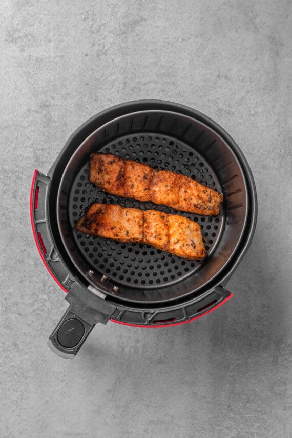 Cooked salmon fillets in an air fryer basket.