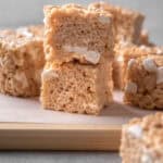 Brown butter rice krispie treats stacked on a wooden cutting board.