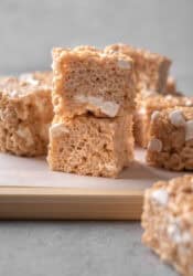 Brown butter rice krispie treats stacked on a wooden cutting board.