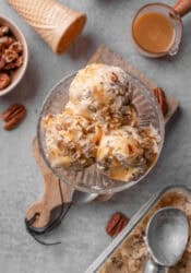Overhead view of scoops of butter pecan ice cream in a glass dessert bowl, surrounded by ingredients.