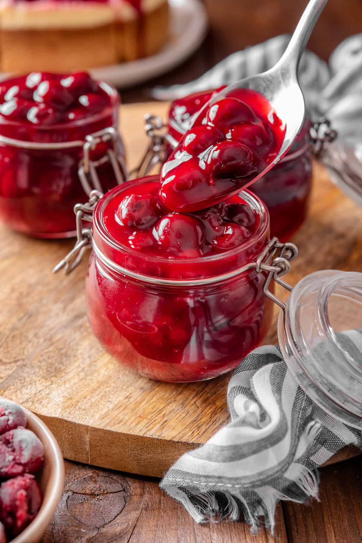 A spoon dripping cherry pie filling into a jar, with more jars of pie filling in the background.