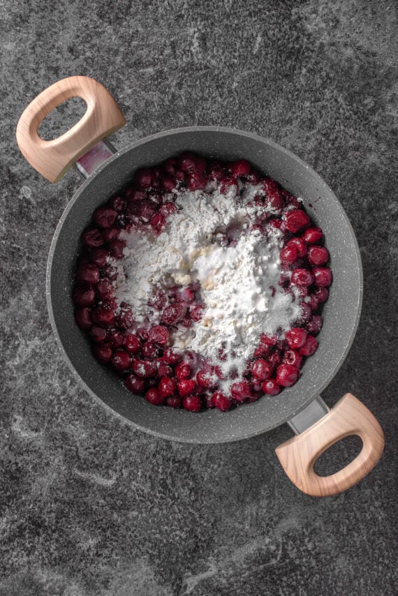 Sugar and other ingredients added to cherries in a pot.