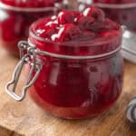 Close up of open jars of cherry pie filling on a round wooden tray.