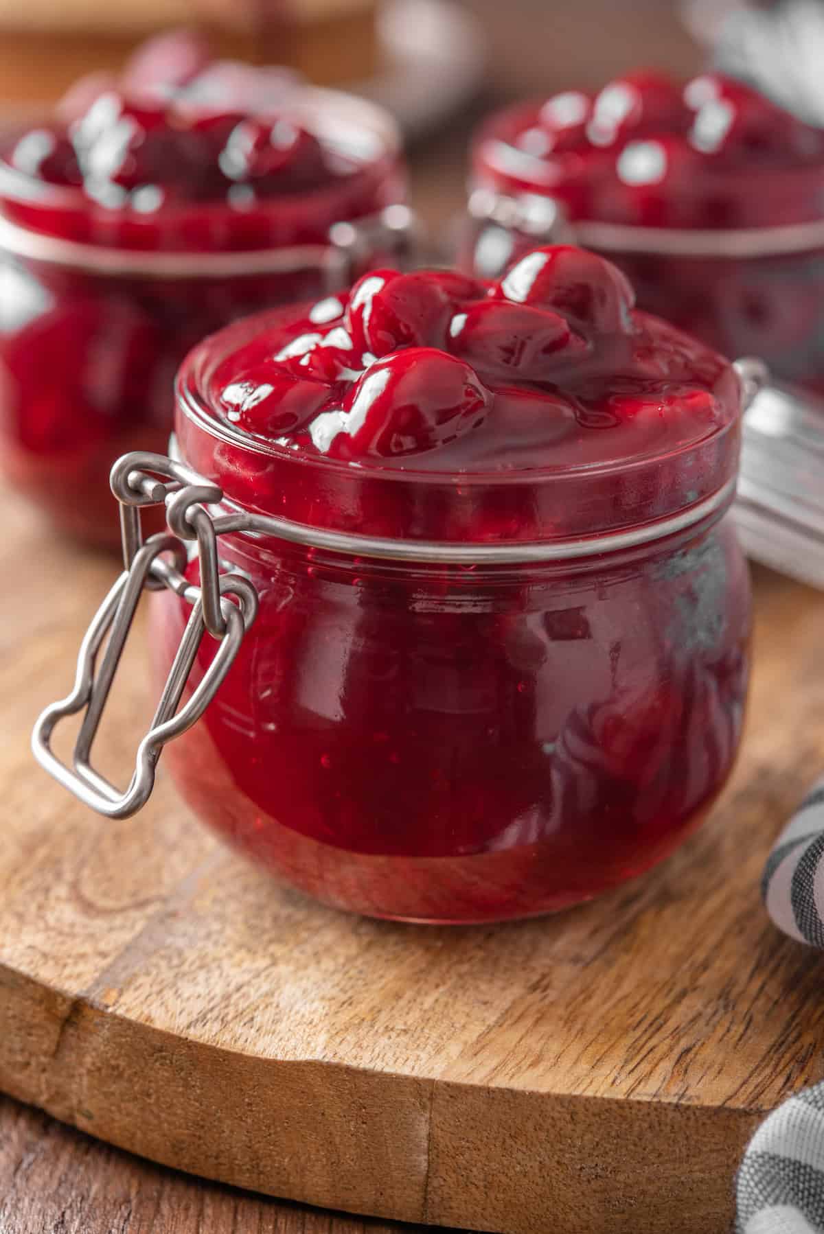 Close up of open jars of cherry pie filling on a round wooden tray.