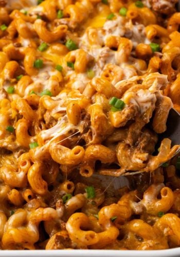 Close up of a spoon scooping cheeseburger casserole from a ceramic baking dish.