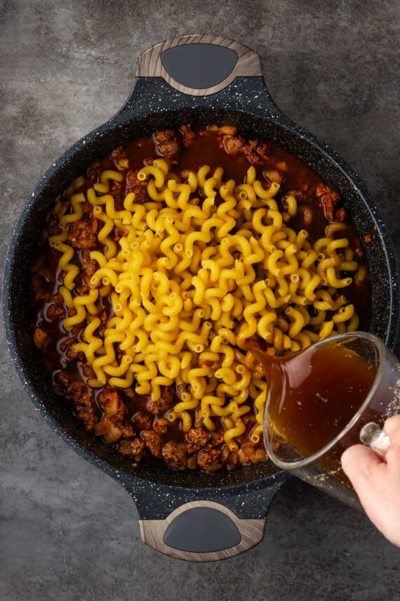 Pasta and broth added to ground beef mixture in a skillet.