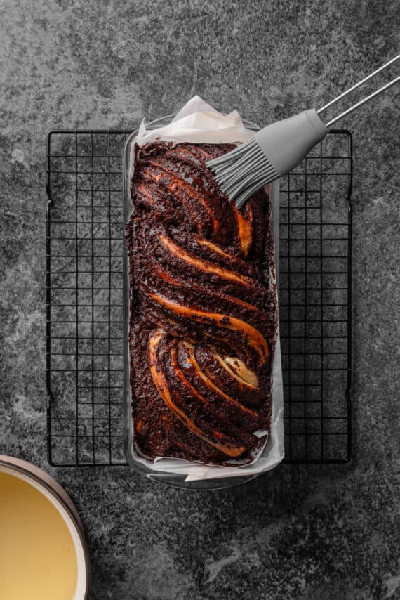 A rubber basting brush coating the top of a chocolate babka with honey water.