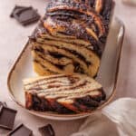 A chocolate babka on a long plate with a slice cut from the end.