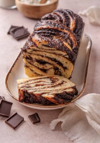 A chocolate babka on a long plate with a slice cut from the end.