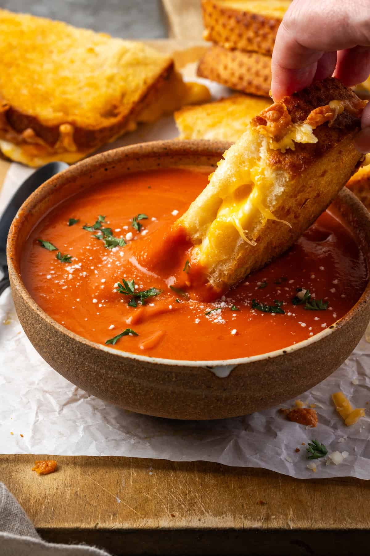 A hand dipping a slice of air fryer grilled cheese into a bowl of tomato soup.