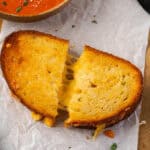 Overhead view of an air fryer grilled cheese cut in half next to a bowl of tomato soup.