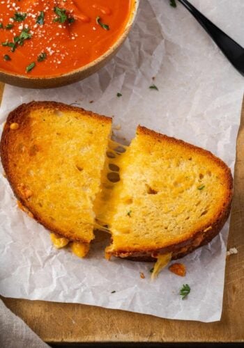 Overhead view of an air fryer grilled cheese cut in half next to a bowl of tomato soup.