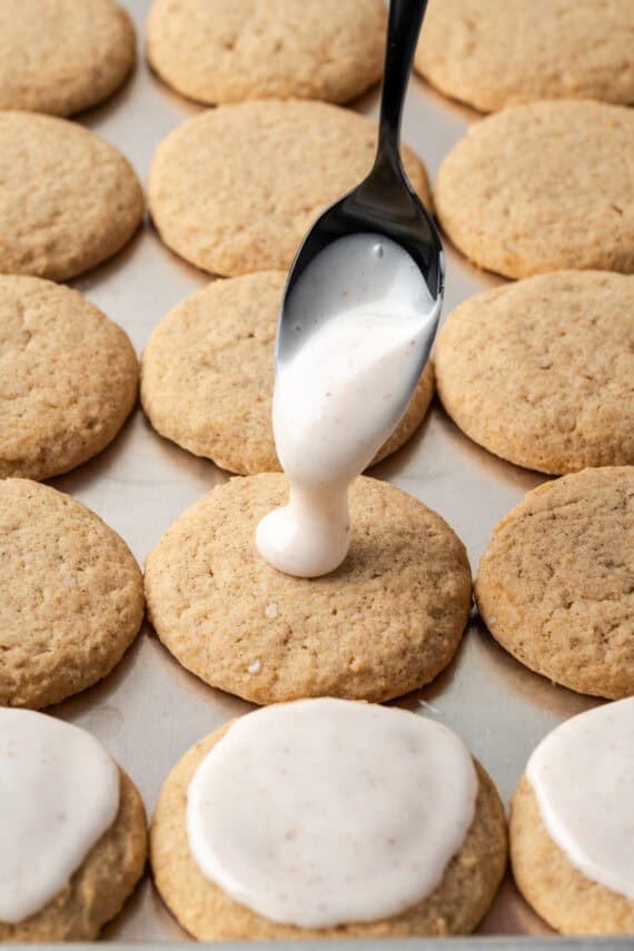 A spoon dripping icing over chai sugar cookies on a baking sheet.