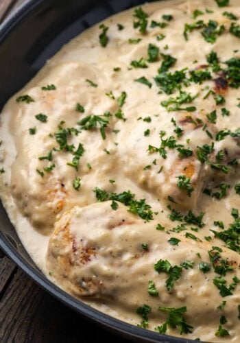 Garlic parmesan chicken in a skillet covered with sauce and garnished with chopped parsley.