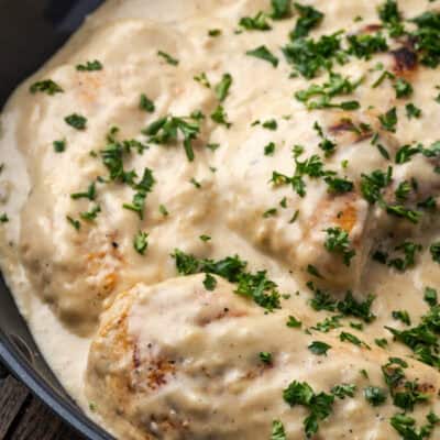 Garlic parmesan chicken in a skillet covered with sauce and garnished with chopped parsley.