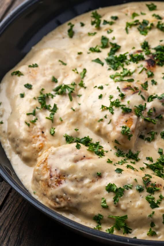 Garlic parmesan chicken in a skillet covered with sauce and garnished with chopped parsley.