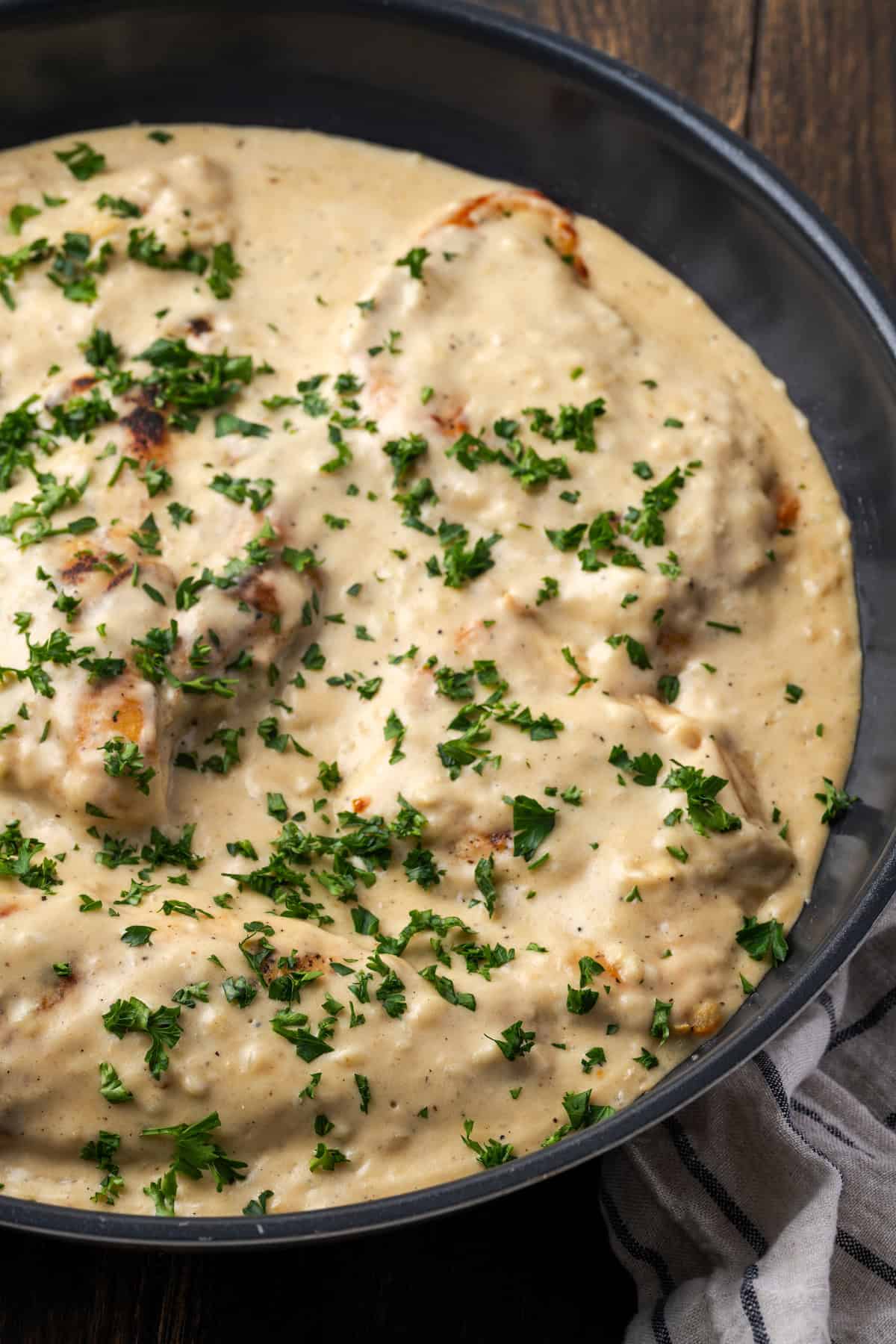 Garlic parmesan chicken in a skillet covered with sauce and garnished with chopped parsley.