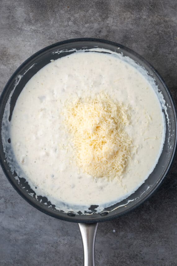 Grated parmesan added to the white sauce in a skillet.