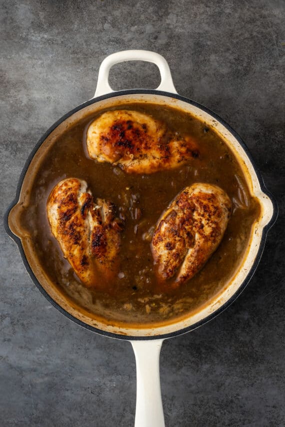 Cooked chicken breasts in a skillet with onion gravy.