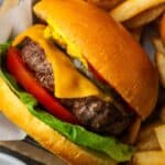 Overhead view of an air fryer burger topped with lettuce, tomato, and cheese in a basket next to fries.