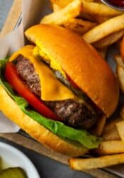 Overhead view of an air fryer burger topped with lettuce, tomato, and cheese in a basket next to fries.