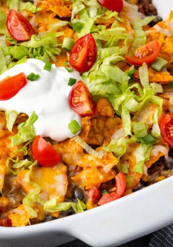 Taco casserole topped with a dollop of sour cream in a ceramic baking dish.