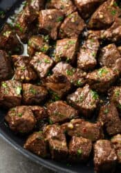 Close up of air fryer steak bites tossed in garlic butter sauce in a skillet.