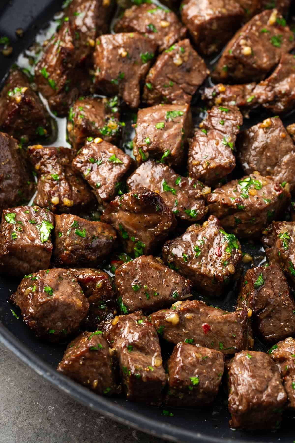 Close up of air fryer steak bites tossed in garlic butter sauce in a skillet.