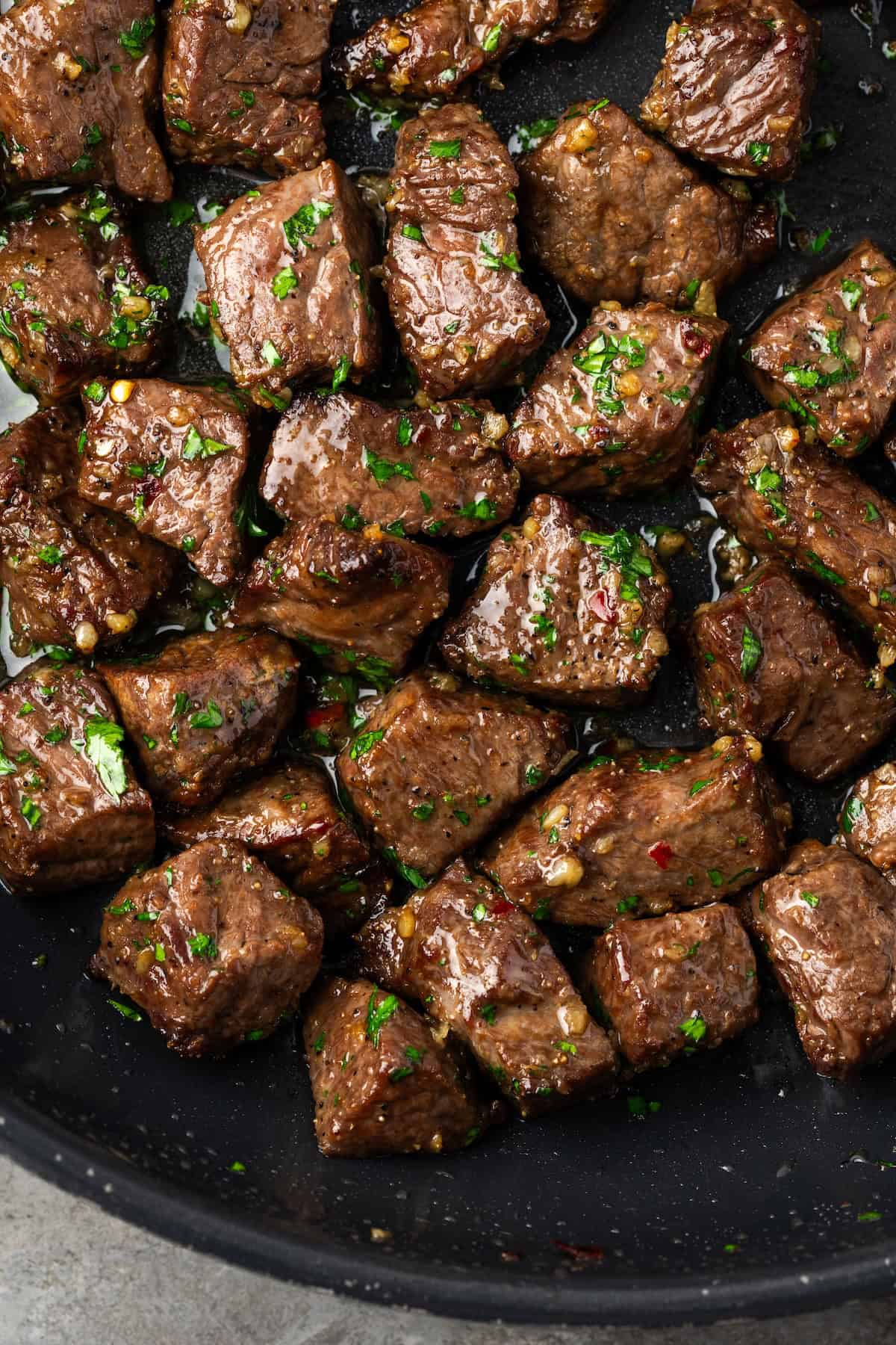 Overhead view of air fryer steak bites tossed in garlic butter sauce in a skillet.