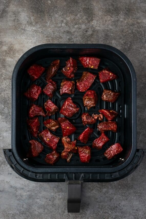 Overhead view of seasoned steak bites arranged inside the air fryer basket.