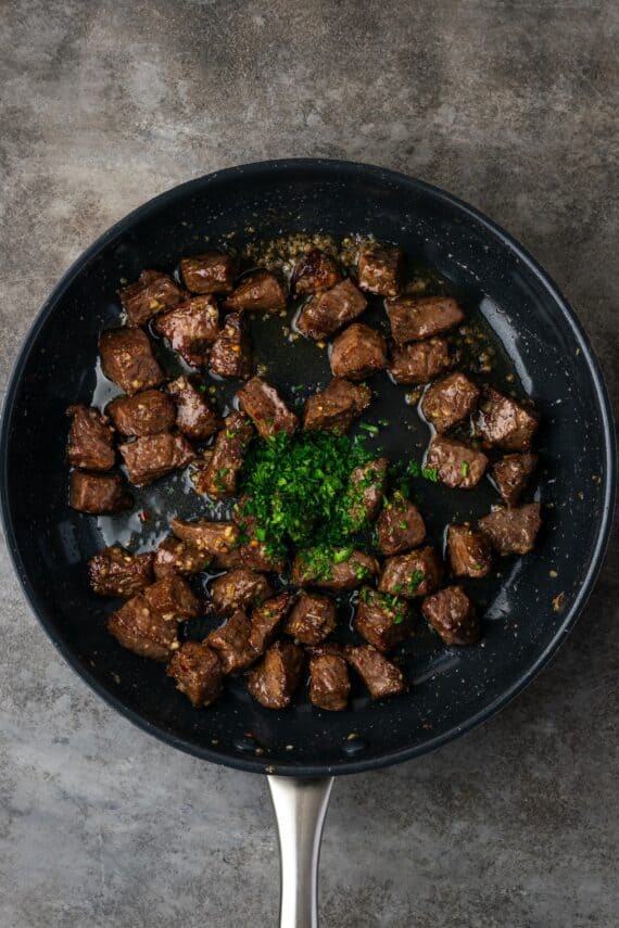 Overhead view of chopped parsley added to a skillet of garlic butter air fryer steak bites.