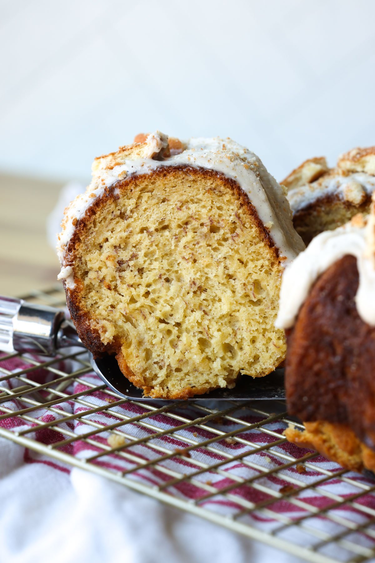 A slice of banana cake with a serving knife on a wire rack