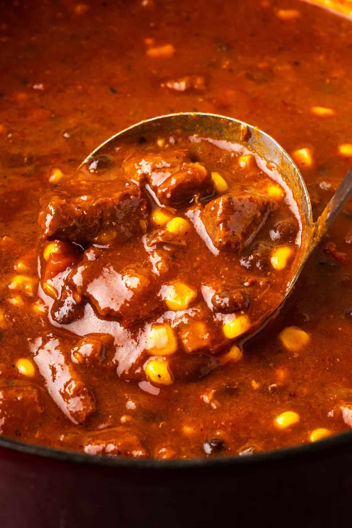 Close up of a ladle scooping chili con carne from a pot.
