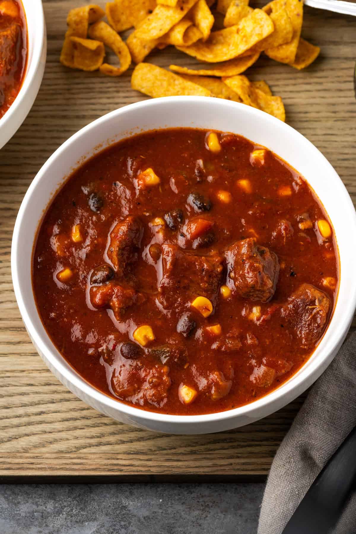 Overhead view of a bowl of chili con carne next to Fritos corn chips on a wooden platter.