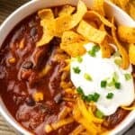 Overhead view of a bowl of chili con carne topped with sour cream and Fritos chips.