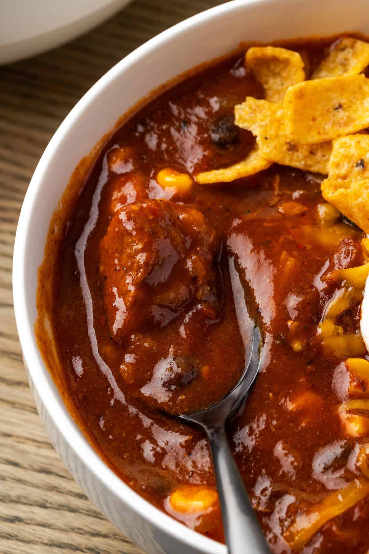 Overhead close up view of a spoon resting in a bowl of chili con carne topped with Fritos chips.