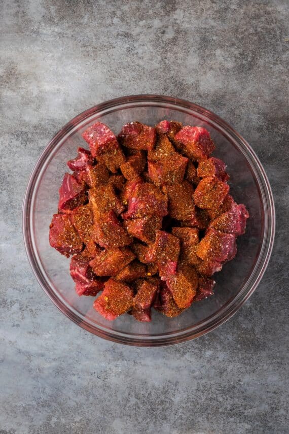 Beef chunks sprinkled with seasonings in a bowl.