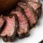 Close up of air fryer filet mignon cut into slices next to a baked potato on a plate.
