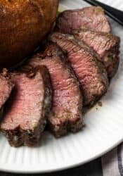 Close up of air fryer filet mignon cut into slices next to a baked potato on a plate.