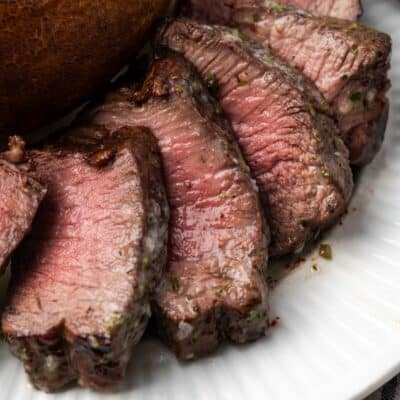 Close up of air fryer filet mignon cut into slices next to a baked potato on a plate.