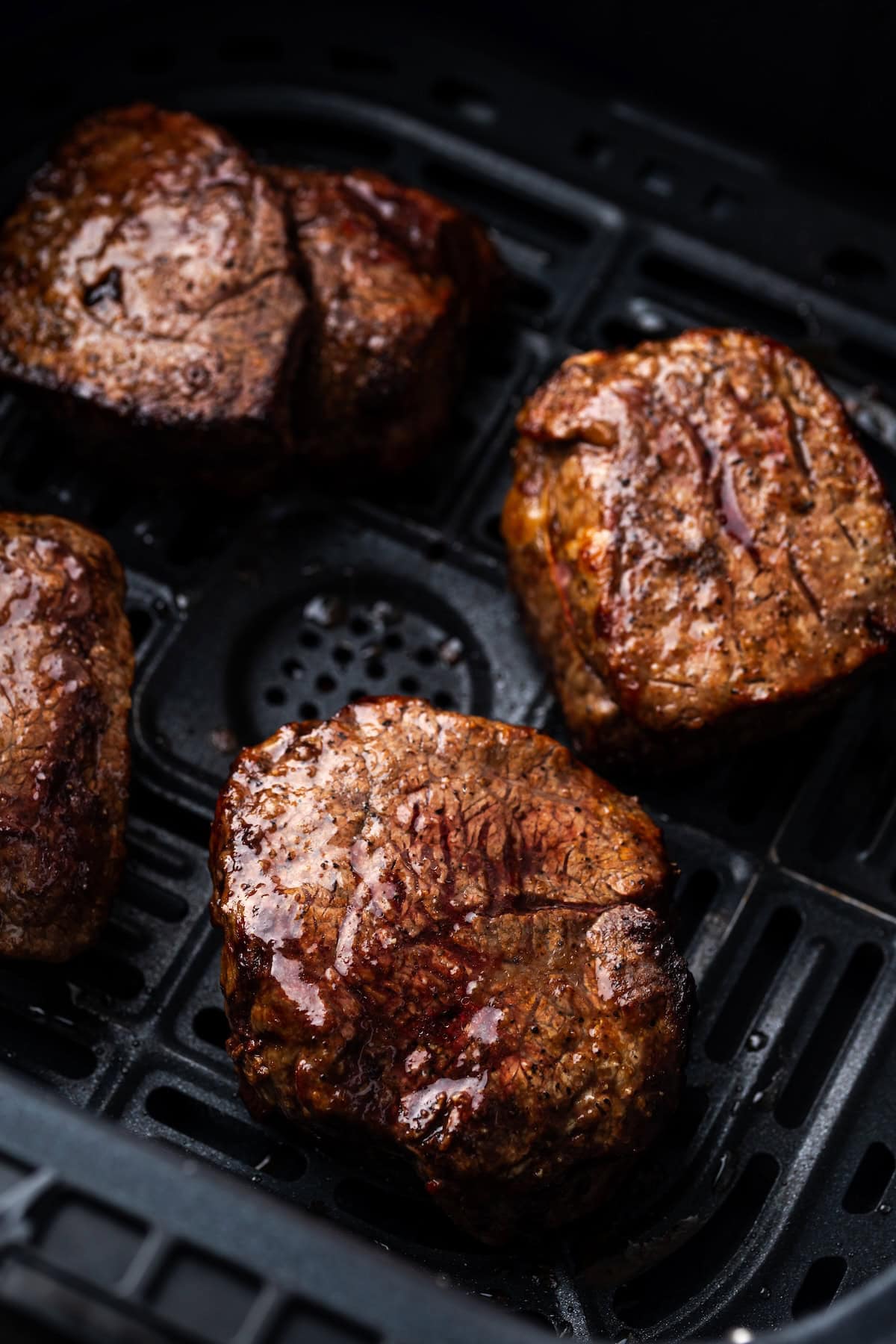 Make juicy, restaurant-quality air fryer filet mignon slathered with homemade garlic compound butter for the ultimate steak dinner! Close up of cooked filet mignon steaks inside the air fryer basket.