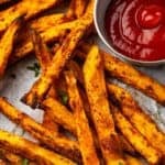 Close up overhead view of air fryer sweet potato fries on a parchment-lined plate next to a ramekin of ketchup.