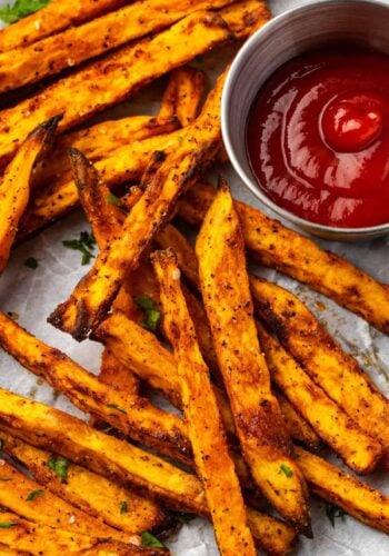Close up overhead view of air fryer sweet potato fries on a parchment-lined plate next to a ramekin of ketchup.