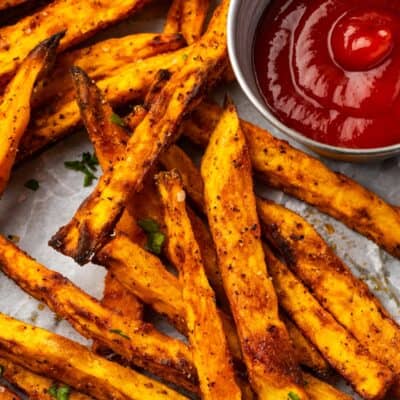 Close up overhead view of air fryer sweet potato fries on a parchment-lined plate next to a ramekin of ketchup.