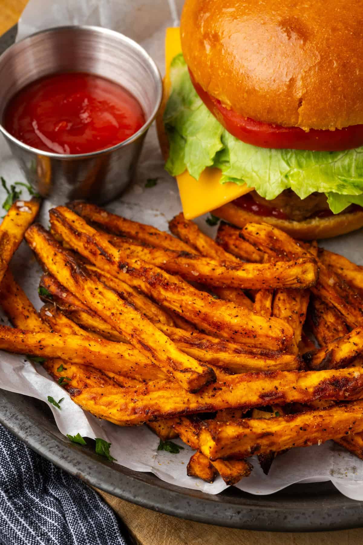 Seasoned with garlic and paprika, crispy air fryer sweet potato fries are tasty and easy to make. It's quicker and lighter than deep frying! Air fryer sweet potato fries served next to a cheeseburger and a ramekin of ketchup on a parchment-lined plate.