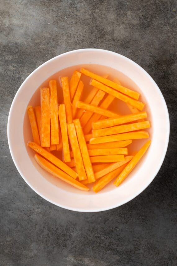 Seasoned with garlic and paprika, crispy air fryer sweet potato fries are tasty and easy to make. It's quicker and lighter than deep frying! Cut sweet potatoes soaking in a bowl of water.
