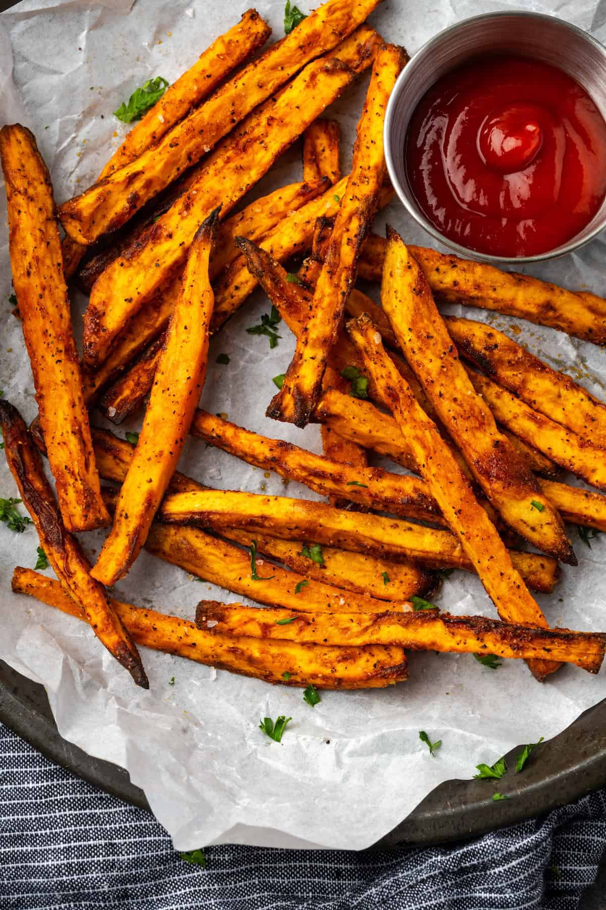 Seasoned with garlic and paprika, crispy air fryer sweet potato fries are tasty and easy to make. It's quicker and lighter than deep frying! Overhead view of air fryer sweet potato fries on a parchment-lined plate next to a ramekin of ketchup.