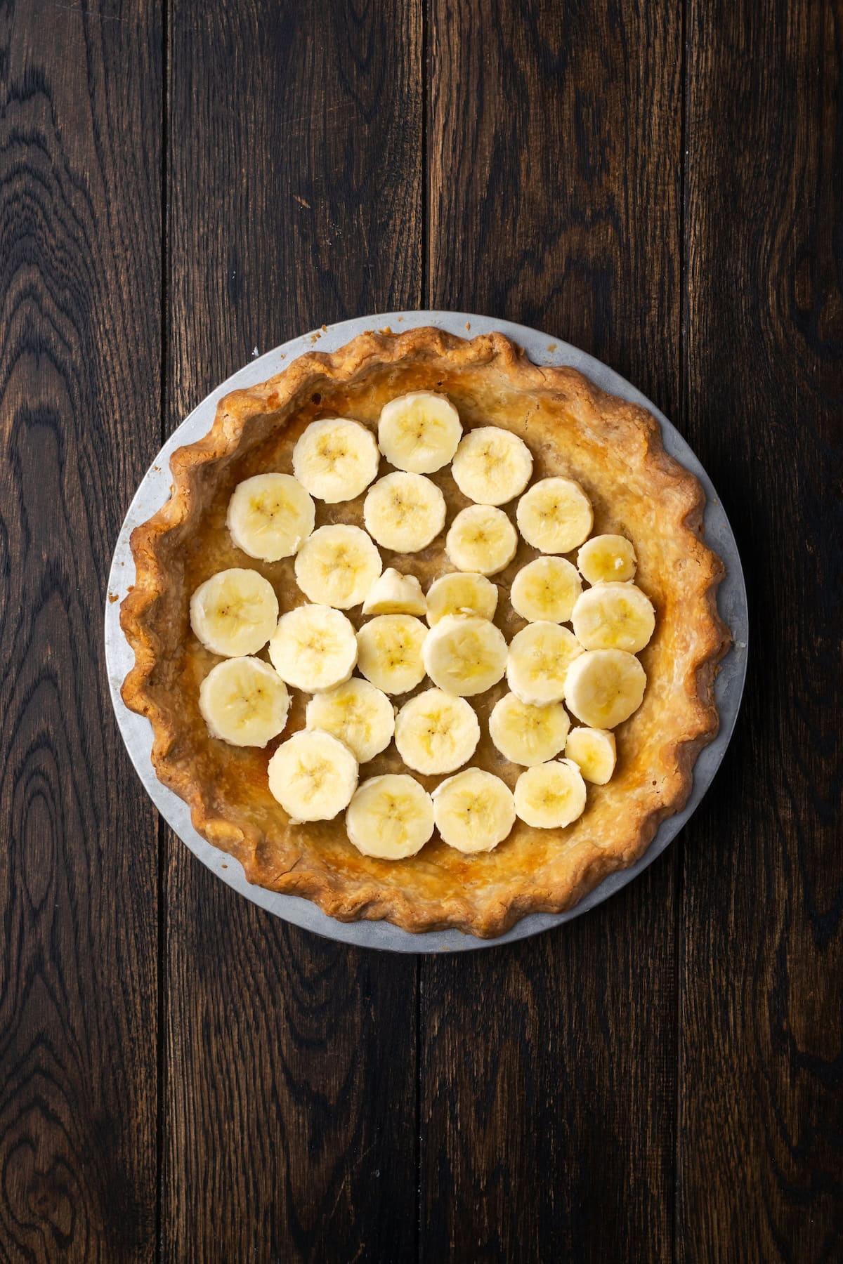 Banana slices arranged in the bottom of a par-baked pie crust.