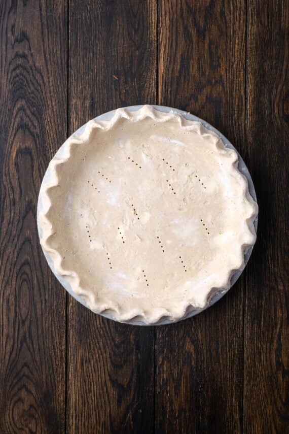 This banana cream pie recipe is a classic dessert with a rich vanilla custard layered with heaps of whipped cream and sweet banana slices. Pie crust pricked with a fork in a pie plate.