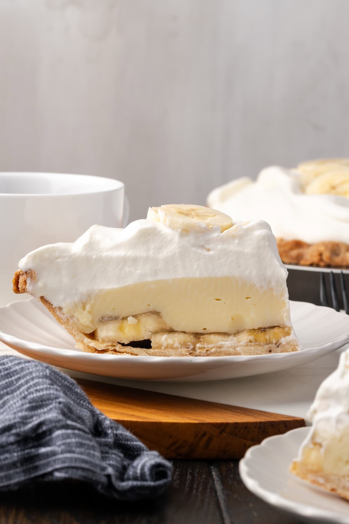 This banana cream pie recipe is a classic dessert with a rich vanilla custard layered with heaps of whipped cream and sweet banana slices. Side view of a slice of banana cream pie on a plate.